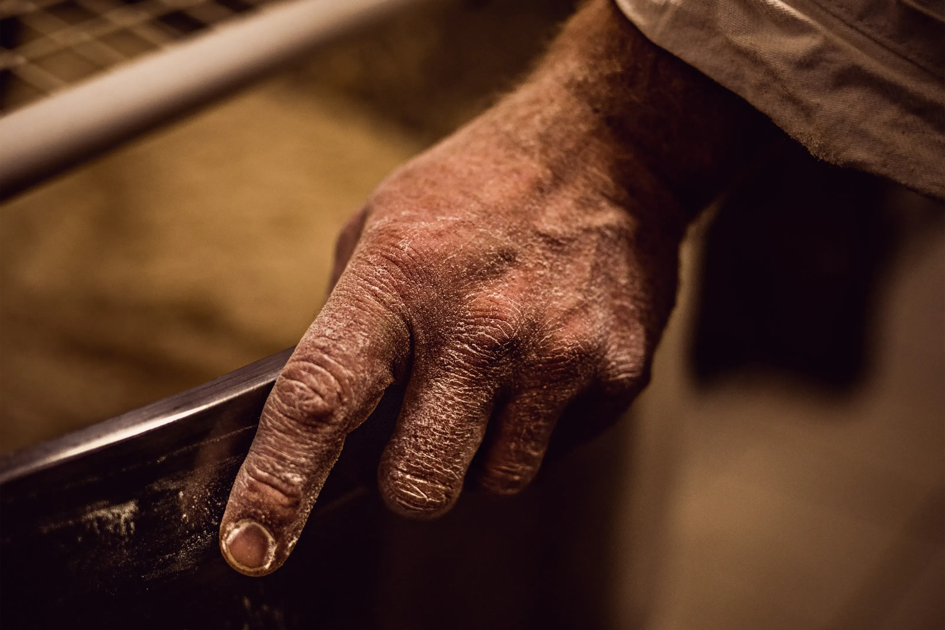 Main d’artisan couverte de farine posée sur le bord d’un pétrin.