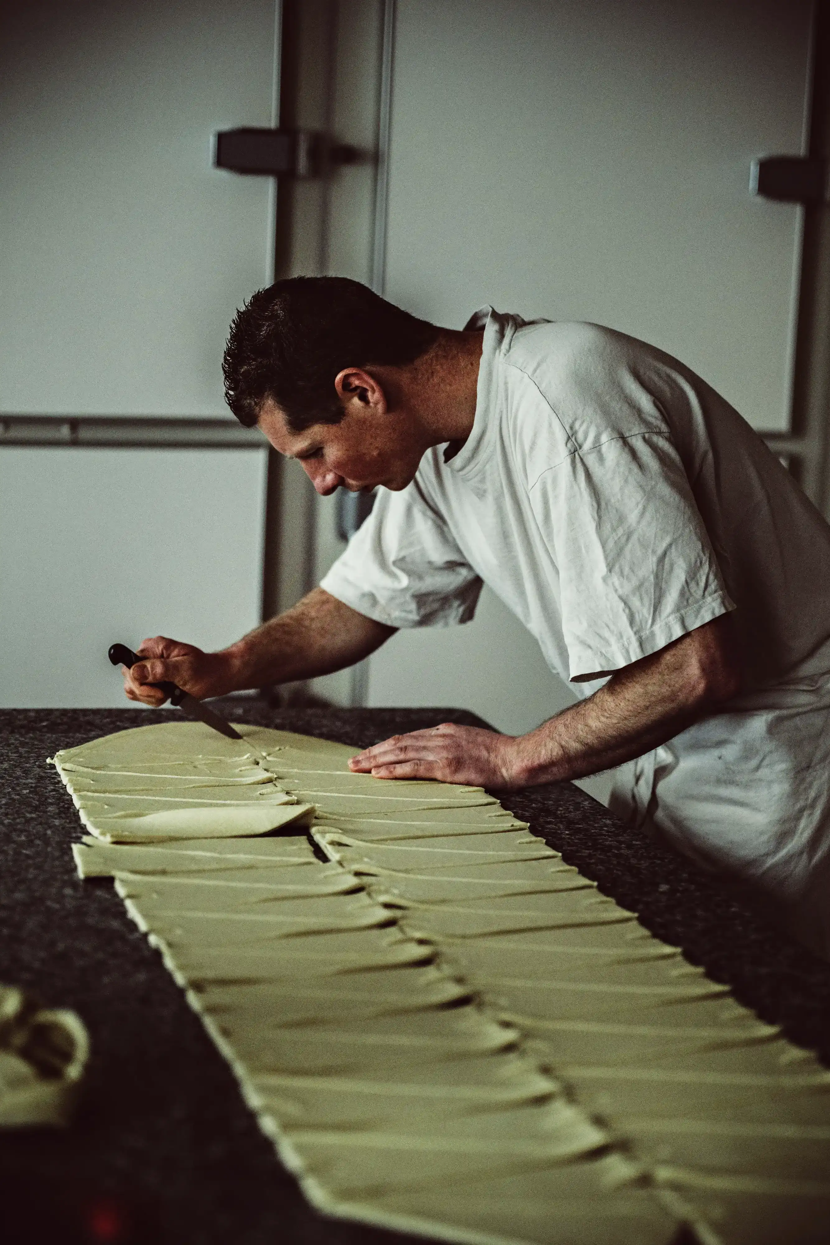 Un artisan boulanger découpe la pâte feuilletée en triangles réguliers, étape préparatoire avant le façonnage des croissants.