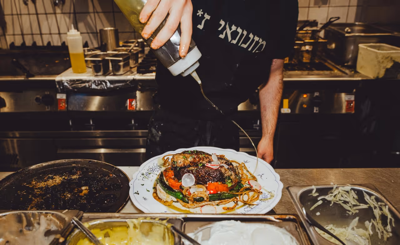Miznon chef plating a seasonal dish in the open kitchen
