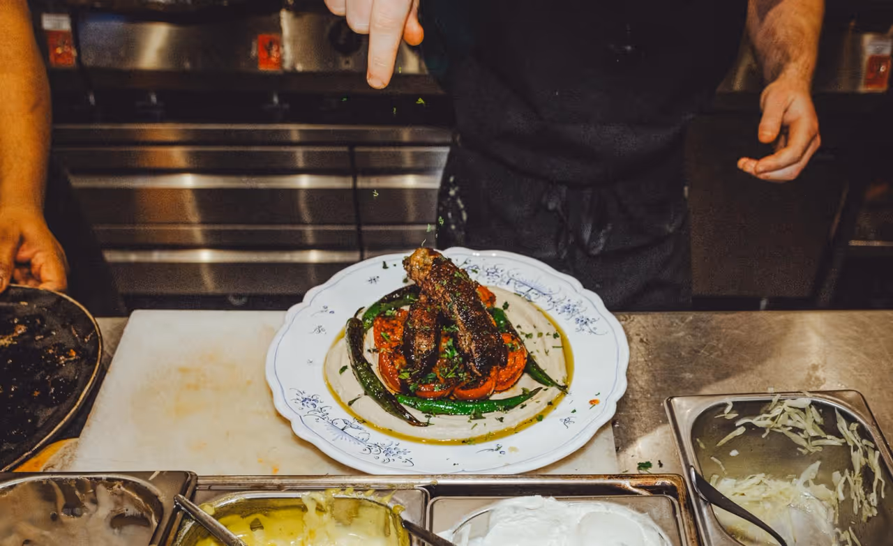 Chef seasoning a grilled lamb dish at Miznon London