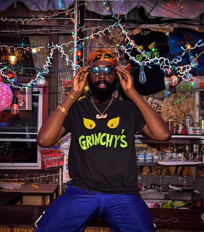 A man with a beard wearing a Grinchy's t-shirt and sunglasses at Roberta's Pizza restaurant.