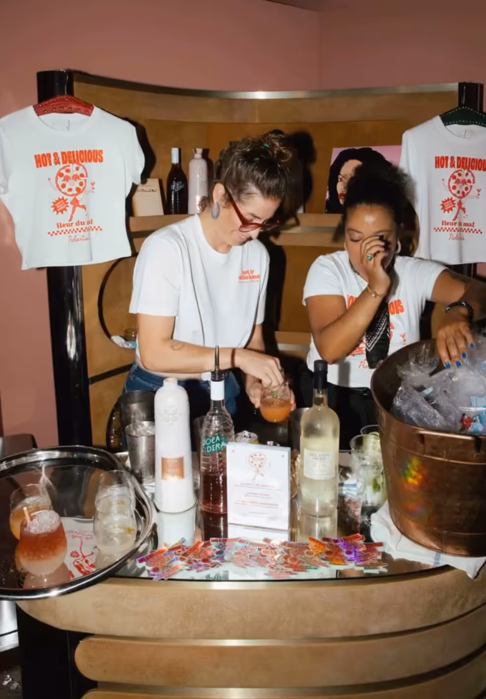 Bartenders preparing cocktails next to "Hot & Delicious" branded t-shirts at Roberta’s Pizza restaurant.